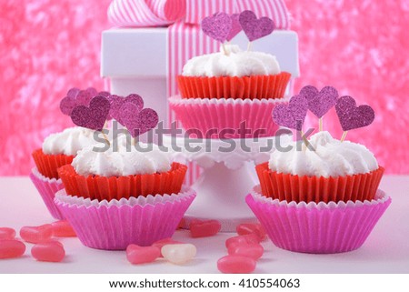 Pink and white cupcakes with heart shape toppers on white wood table with pink background for Mothers Day, Valentine or feminine birthday celebration. 