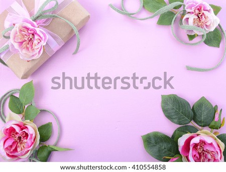 Pale pink feminine background with gift and silk roses on wood table with decorated borders, for Mothers Day, Valentine or feminine birthday or anniversary with copy space. 