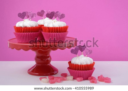 Pink and white cupcakes with heart shape toppers on white wood table with pink background for Mothers Day, Valentine or feminine birthday celebration. 