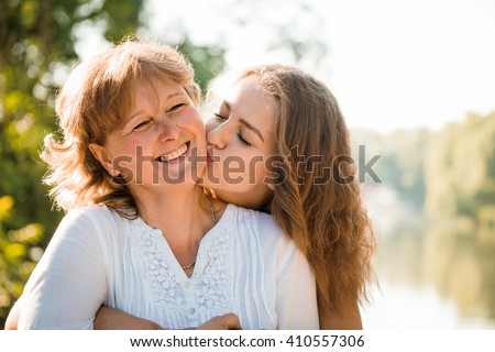 Teenage girl hugging and kissing her mother h outdoor in nature on sunny day