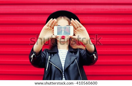 Fashion glamour woman makes self portrait on smartphone blowing lips over city pink background