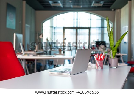 Working Place on grey Table with Laptop Computer green Flower red Chair and Pencils in modern Office interior with large Window on Background Royalty-Free Stock Photo #410596636