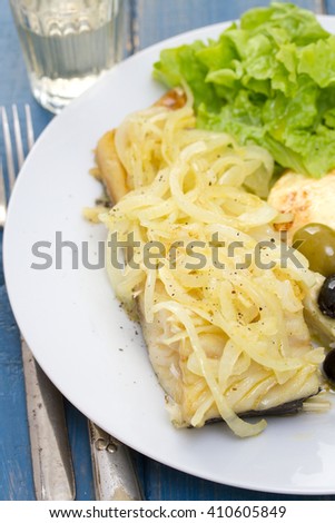 cod fish with onion, mashed potato and salad on white plate on blue wooden background