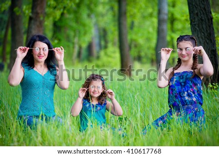 A close up family picture of two daughters on either side of their mother each giving a kiss on her cheek.