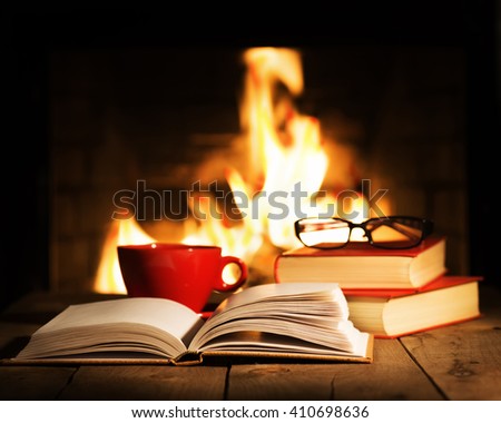 Red cup of coffee or tea, glasses and old books on wooden table near fireplace. Winter and Christmas holiday concept. Royalty-Free Stock Photo #410698636