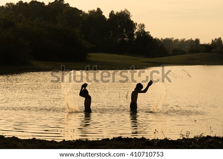 boys silhouette are playing water in the river during sunset.