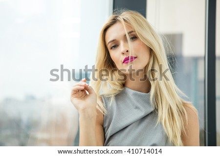 close portrait of a beautiful blonde woman near a large window from an office building