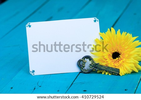 Blank note card and house key by yellow sunflower on antique rustic teal blue wood background; white copy space