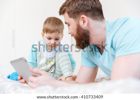 Father and son lying and playing with tablet at home