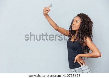 Afro american woman making selfie photo on smartphone over gray background
