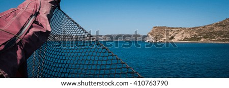 Boat view of a cliff in the sea with a building on top of it with a net in the front of the picture in Greece