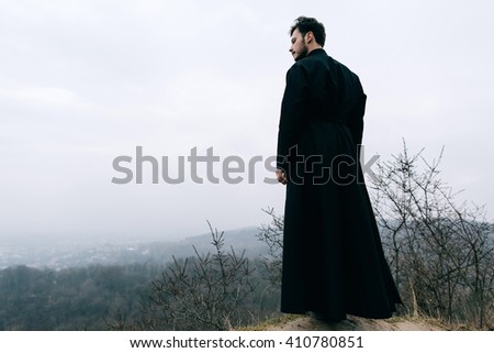 Portrait of handsome catholic bearded priest or pastor posing outdoors in mountains.
City.  Royalty-Free Stock Photo #410780851