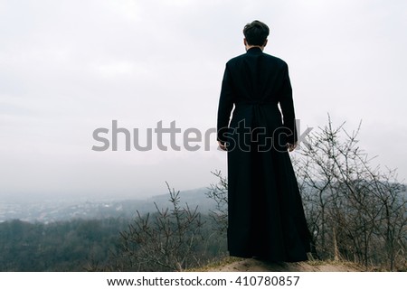 Portrait of handsome catholic bearded priest or pastor posing outdoors in mountains.
City.  Royalty-Free Stock Photo #410780857