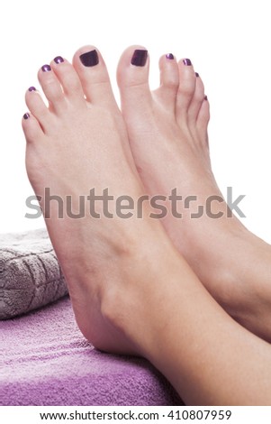 Bare feet with pedicure propped by towel on soft purple treatment table against white background