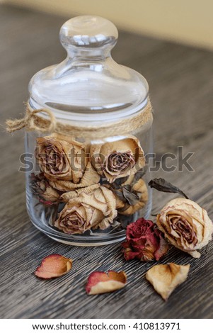 Dried pink roses heads in glass jar and petals on rustic wooden table. 