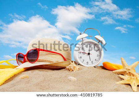 Beach accessories with alarm clock on the beach in the sand against the blue sky with clouds. Summer vacation concept Royalty-Free Stock Photo #410819785