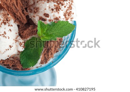 Close up of vanilla ice cream balls, covered with chocolate biscuits, grated chocolate and fresh mint leafs in the blue glass isolated over white background. Top view, selective focus.
