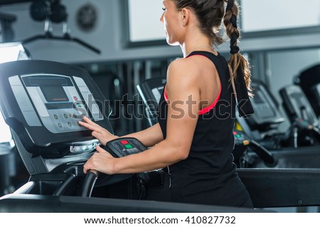 Young female athlete exercising on treadmill in modern gym, setting up difficulty level.