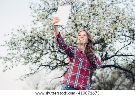 Happy woman taking selfie on tablet in the blooming garden. Leisure in spring day. Toned image
