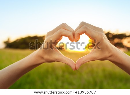 Hand shaped heart against a beautiful sunset.  Royalty-Free Stock Photo #410935789