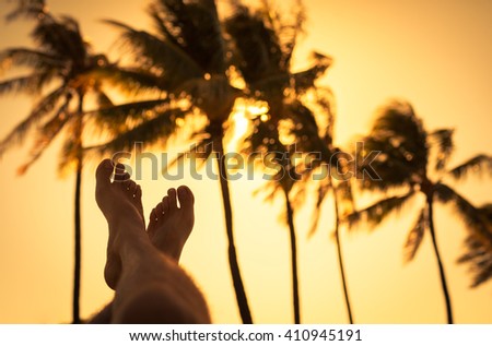 Sit back and relax. Pair of feet relaxing against palm trees swaying in the wind.