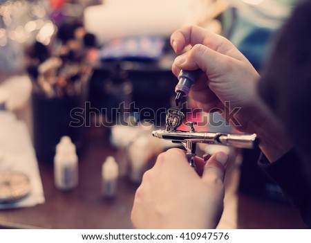 Make up artist filling airbrusher with liquid paint.Professional body art painting with air brush device.Beauty salon treatment Royalty-Free Stock Photo #410947576