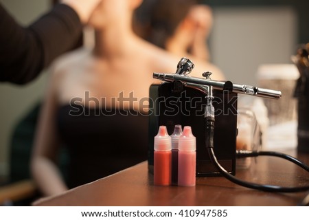 Makeup airbrush & bottles with liquid paint for body art.Visagiste table in beauty studio.Model being painted on background in salon Royalty-Free Stock Photo #410947585