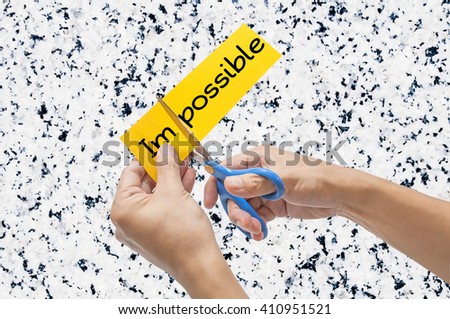 Hand with a scissors cutting yellow paper isolated on white granite background. Changing the word impossible to possible concept.