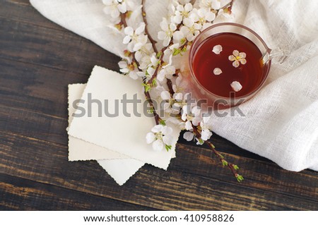 Cup of tea, empty old photo and blossoming apricot branch on a wooden table