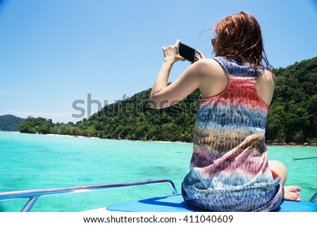 Woman traveler photographing sea island view with smart phone on boat , Thailand