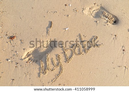 written words "My babe" on sand of beach by  footprints around