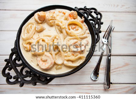 Tasty seafood in white sauce on a metal black plate. Top view