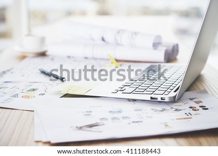 Sideview of laptop placed on wooden table with sketches on paper
