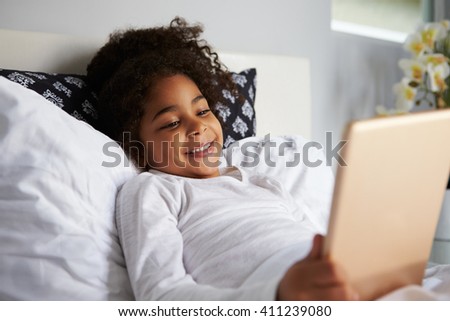 Smiling young girl lies in bed uses digital tablet, close up