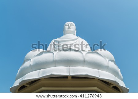 Horizontal picture of white statue of Buddha in Long Son Pagoda in Nha Trang, Vietnam, sitting on lotus by background of blue sky (bottom view)