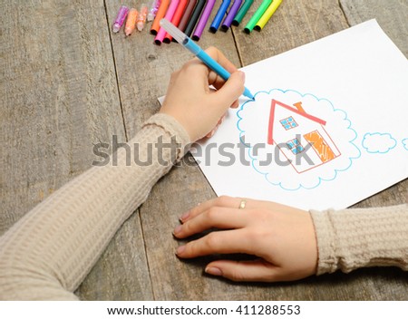 A woman hand with pencil is drawing picture of country house