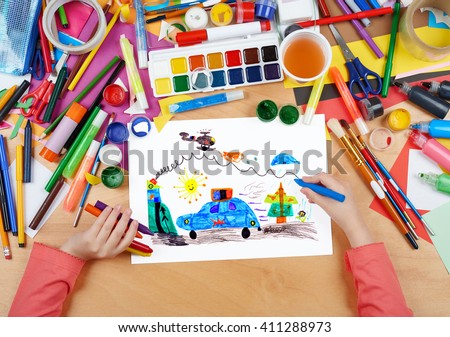 child drawing police car and helicopter, top view hands with pencil painting picture on paper, artwork workplace