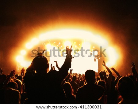 Silhouettes of cheering people at rock concert in front of stage illuminated with spotlights Royalty-Free Stock Photo #411300031