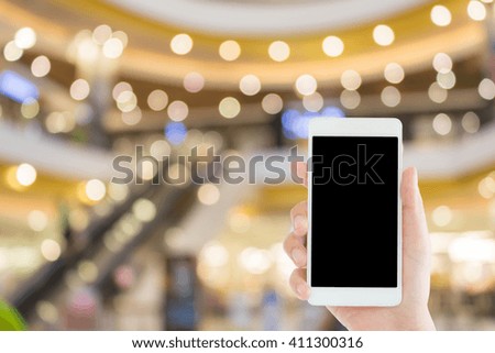 woman use mobile phone and blurred image of people in the mall with escalator and beautiful bokeh