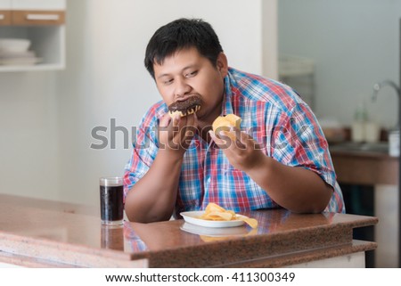 The fat guy is eating his junk food. This picture take by soft skin tone and selective focus on face of model.