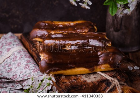 Eclairs with chocolate glaze on wooden board with spring flowers. Toned image selective focus