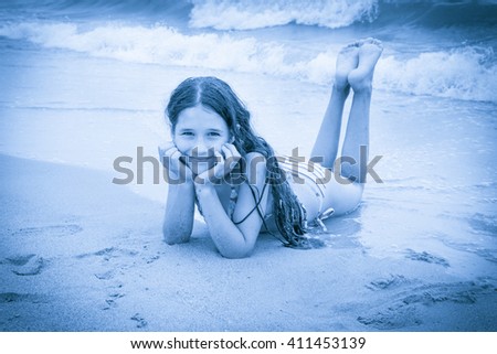 Smiling girl on the beach lying down on the sand near water, blue toned picture