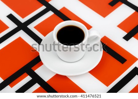 View of a cup with black drink inside on a black and white and red background.