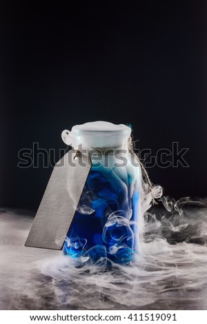 Vintage glass jar with a blue liquid with dry ice on a dark background. blank tag inscription