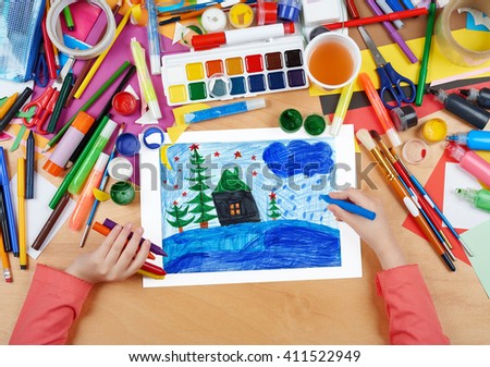 child drawing christmas night in forest with house , top view hands with pencil painting picture on paper, artwork workplace