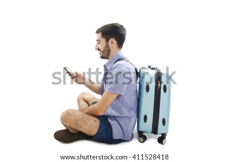 Tourist sitting against a suitcase and using a mobile phone. Isolated on a white background 