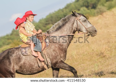 two young happy kids riding a horse on farm, outdoor portrait on rural background