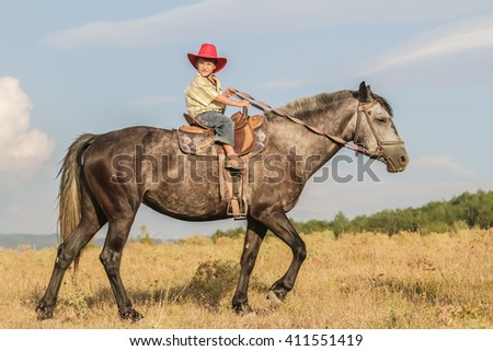 outdoor portrait of young happy boy riding a horse on farm, rural background