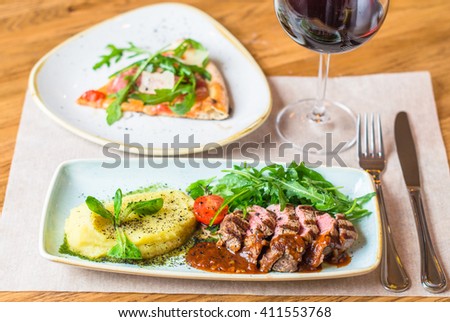 
Beef steak with arugula , vegetable puree, pizza and wine. Close-up on the plate on the served table . Italian restaurant.
