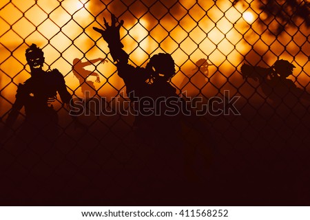 Several zombie behind a mesh fence at night.